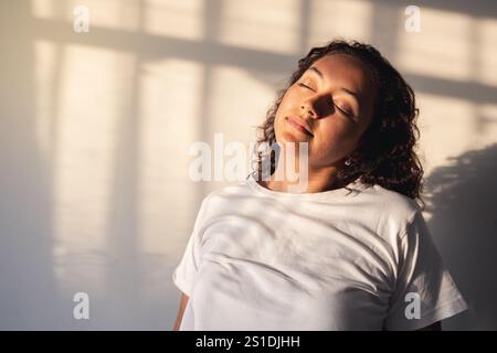 Femme avec les yeux fermés appréciant les rayons du soleil dans la maison au coucher du soleil Banque D'Images