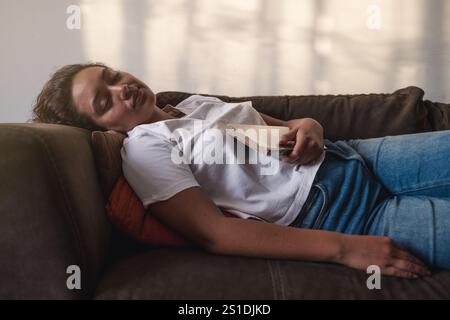 Jolie femme sieste sur le canapé dans son salon après avoir refait le livre Banque D'Images