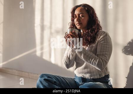 Jeune femme latine appréciant et buvant du café dans le salon Banque D'Images