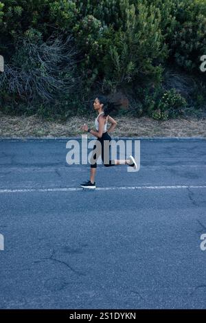Vue latérale de toute la longueur de la femelle mince courir sur une route abandonnée dans un parc naturel. Femme pratiquant la course à l'extérieur. Vue latérale sur toute la longueur de Banque D'Images
