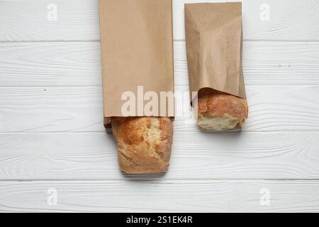 Sacs en papier avec baguettes fraîches sur table en bois blanc, vue de dessus Banque D'Images