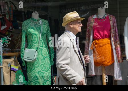 Aberystwyth Royaume-Uni - 2 août 2024 ; un homme âgé bien habillé en costume et chapeau marche devant la vitrine des vêtements de w OMEN. Banque D'Images