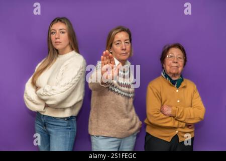 Trois femmes d'âges différents debout ensemble sur fond violet, montrant le symbole féminin dessiné sur la main et revendiquant l'égalité et les droits des femmes Banque D'Images