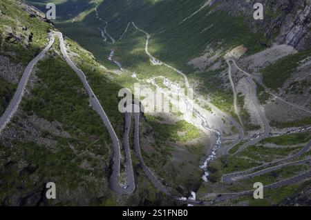 Une route sinueuse serpente à travers une vallée verdoyante entre montagnes escarpées, Trollstigen, Andalsnes, Norvège, Europe Banque D'Images