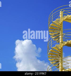 Escalier extérieur en colimaçon peint en jaune vif contre un ciel bleu acier. Format carré. Escalier extérieur en colimaçon peint en jaune vif contre un montant Banque D'Images