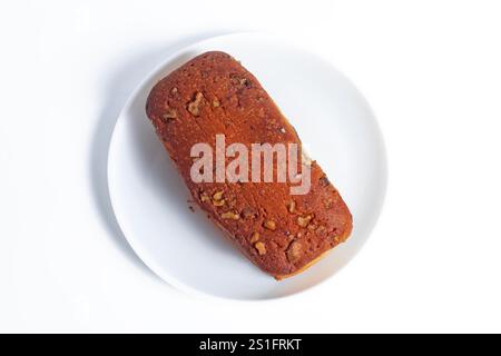 Un délicieux pain à la banane fraîchement cuit surmonté de noix croquantes, élégamment présenté sur une assiette blanche. parfait pour les promotions de boulangerie. Banque D'Images