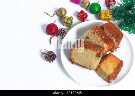 Délicieuses tranches de gâteau servies sur une assiette blanche, entourées de décorations de Noël festives comprenant des pommes de pin, des boules colorées et des boîtes cadeaux. p Banque D'Images