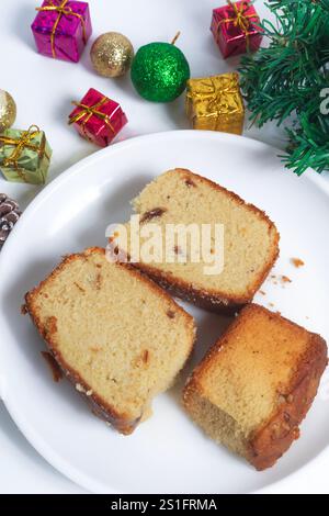 Délicieuses tranches de gâteau servies sur une assiette blanche, entourées de décorations de Noël festives comprenant des pommes de pin, des boules colorées et des boîtes cadeaux. p Banque D'Images