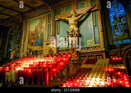 Basilique notre-Dame autel Christ Crucifié Montréal // MONTRÉAL, Canada — Un autel latéral à la Basilique notre-Dame de Montréal présente une sculpture du Christ Crucifié. Des rangées de bougies votives rouges et blanches brûlent devant l'exposition religieuse. L'espace de dévotion intime permet aux visiteurs et aux paroissiens d'allumer des bougies comme offrandes de prière. La basilique notre-Dame est l'un des monuments religieux et historiques les plus importants de Montréal. Banque D'Images
