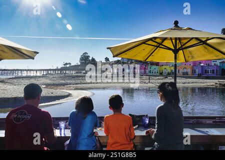 Capitola, Californie États-Unis - 2 janvier 2024 Une famille de touristes regarde les habitants profiter d'une partie de Beach volley devant le célèbre Vene coloré Banque D'Images