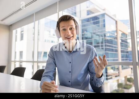 Heureux jeune homme professionnel d'affaires portant des écouteurs, parlant à la caméra Banque D'Images