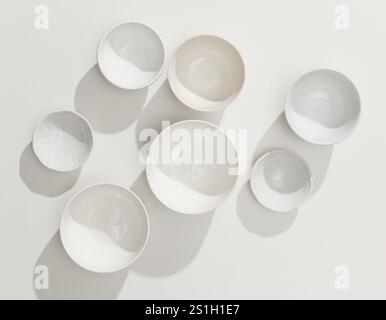 divers bols vides blancs sur fond de table blanc avec des lumières et des ombres ensoleillées, vue de dessus Banque D'Images