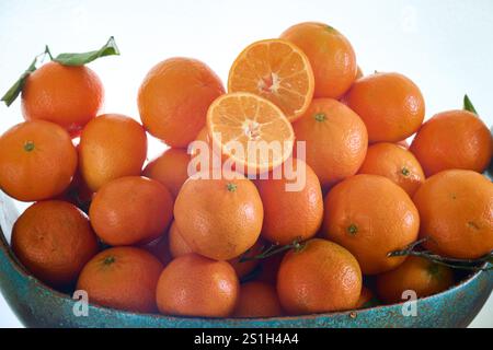 Une orange mandarine coupée en deux sur d'autres mandarines fraîches juste cueillies de l'arbre sur un fond blanc Banque D'Images