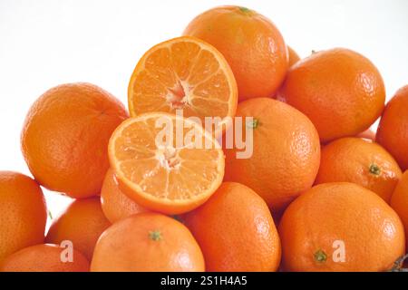 Une orange mandarine coupée en deux sur d'autres mandarines fraîches juste cueillies de l'arbre sur un fond blanc Banque D'Images