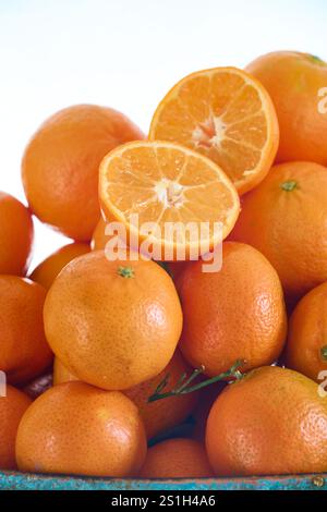 Une orange mandarine coupée en deux sur d'autres mandarines fraîches juste cueillies de l'arbre sur un fond blanc Banque D'Images