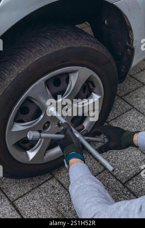 Jeune homme changeant un pneu de voiture sur la route, en utilisant une clé pour dévisser les écrous de roue. Photo de haute qualité Banque D'Images