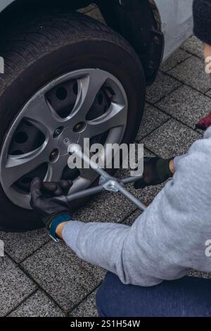 Jeune homme changeant un pneu de voiture sur la route, en utilisant une clé pour dévisser les écrous de roue. Photo de haute qualité Banque D'Images