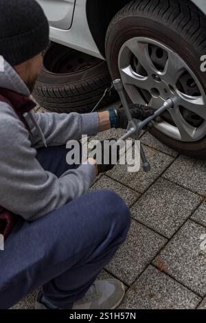 Jeune homme changeant un pneu de voiture sur la route, en utilisant une clé pour dévisser les écrous de roue. Photo de haute qualité Banque D'Images