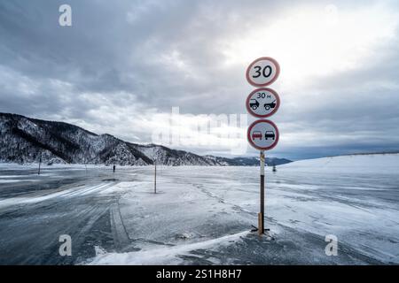 Des panneaux de signalisation sont affichés sur une route gelée dans les montagnes enneigées, avertissant les conducteurs sous un ciel nuageux Banque D'Images