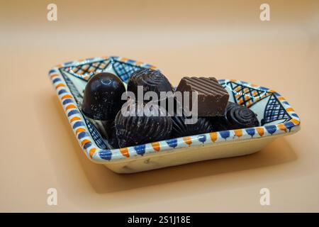 plat en céramique rempli de divers morceaux de chocolat noir, chacun avec différentes formes et textures. Le plat présente un motif coloré et géométrique Banque D'Images
