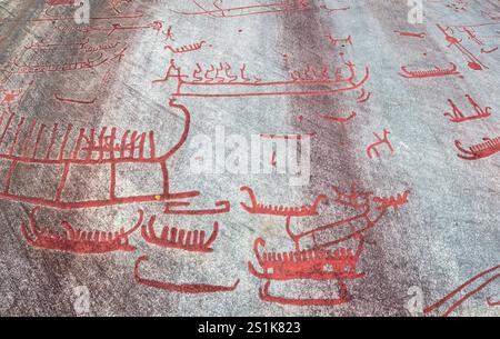 Recopie des sculptures rupestres de Tanum sur la roche plate de Vitlycke, peinte en rouge, représentant des bateaux, des gens et des animaux, datant des âges du bronze et du fer. Banque D'Images