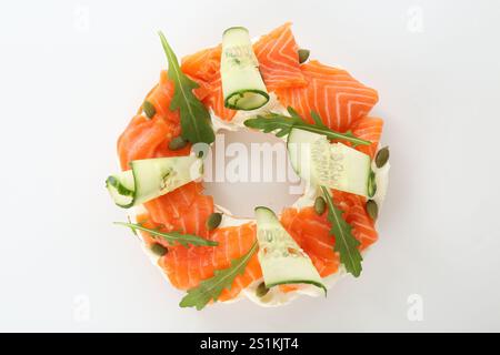 La moitié de délicieux bagel au saumon, fromage à la crème et concombre sur fond blanc, vue de dessus Banque D'Images