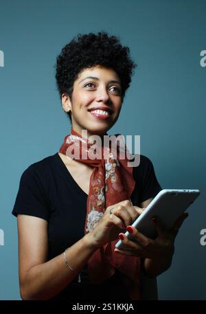 Femme joyeuse peau brune tenant une tablette sur ses mains et regardant vers le haut. Cours de collège, étudiant universitaire, hôtesse d'entreprise. Portrait vertical. Banque D'Images