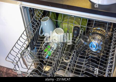 Lave-vaisselle ouvert rempli de verrerie propre, de tasses en céramique et d'assiettes vertes disposées soigneusement sur des supports métalliques. Banque D'Images