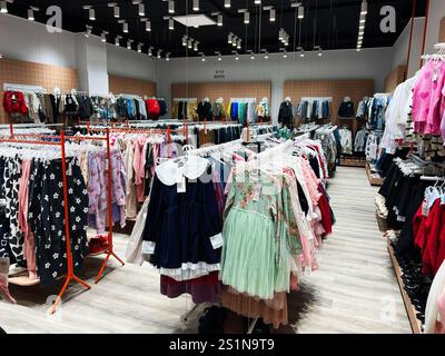 Kiev, Ukraine - 04 janvier 2025 : magasin de vêtements organisé présentant des robes pour enfants, des tenues et des accessoires disposés sur des étagères sous un éclairage moderne. Banque D'Images