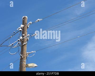 Un vieux poteau électrique en bois avec une lampe et des câbles électriques suspendus après une tempête de neige. Gros plan. Banque D'Images