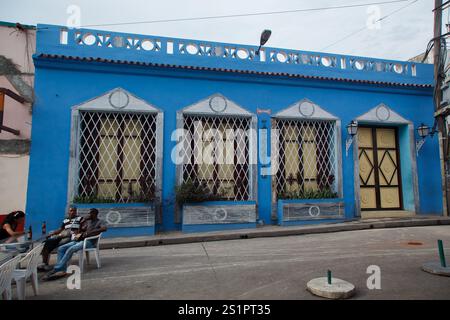Les gens prenant une bière assis devant une façade bleue traditionnelle typique d'un bâtiment colonial sur la Plaza de Dolores, au centre-ville de Santiago de Cuba Banque D'Images