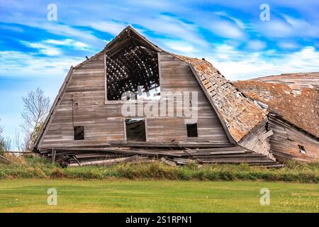 Une grange avec une grande fenêtre ouverte et un toit qui manque quelques bardeaux. La grange est vieille et a un aspect rustique Banque D'Images