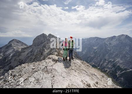 Couple, deux alpinistes avec des casques sur une étroite crête rocheuse, traversant le Jubilaeumsgrat, vue sur les sommets rocheux et Alpspitze, Wetterstein RA Banque D'Images