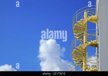 Escalier extérieur en colimaçon peint en jaune vif devant un ciel bleu en acier avec formation dynamique de nuages. Format paysage. Texte peint en jaune vif Banque D'Images