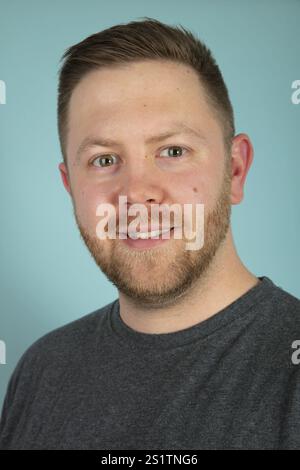 Jeune homme décontracté barbu dans un t-shirt gris regardant pensivement la caméra. Un gros plan portrait frontal de studio Banque D'Images