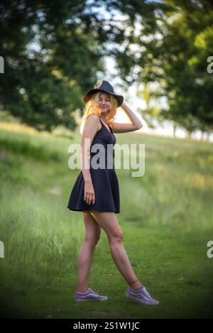 Jeune femme blonde marchant dans la nature un soir d'été portant une robe noire. Jeune femme blonde marchant dans la nature un soir d'été Banque D'Images