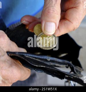 Pauvreté : les doigts d'un vieil homme retirent deux pièces en euros d'un portefeuille usé. Format carré. Pauvreté : les doigts d'un vieil homme sortent deux pièces en euros Banque D'Images
