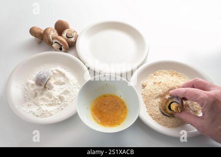 La main d'une femme âgée panant la farine de champignons, l'œuf et la chapelure pour être frits ou cuits au four, cuisiner des collations de légumes, l'espace de copie, s Banque D'Images