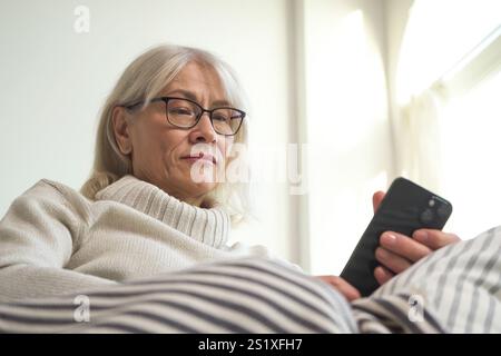 Femme âgée se sentant suspicieuse tout en vérifiant son smartphone Banque D'Images