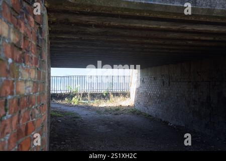 Saleté passage bas à l'ombre sous un pont en béton avec un lac à la fin de la structure Banque D'Images