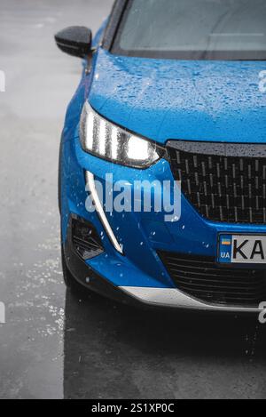 Blue Peugeot 2008 sous forte pluie. Vue rapprochée de la partie avant droite du crossover compact français face à la caméra. Banque D'Images