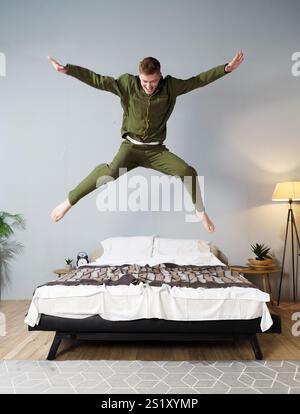 Un homme dans une veste verte saute sur un lit. Le lit est sur un plancher en bois Banque D'Images