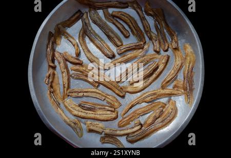 Vue de dessus de bananes déshydratées naturelles sur plateau rond en acier avec fond noir. Délicieuse banane tranchée séchée au soleil, vue de dessus, utilisez-la comme votre Wallpape Banque D'Images