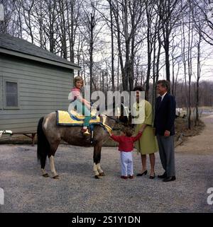 31 mars 1963 le président John F. Kennedy et sa famille regardent Caroline Kennedy monter un cheval nommé 'Tex' à Camp David. 'Tex' porte une selle marocaine bleue et or, un cadeau au président Kennedy du roi Hassan III photographie comprend : (de gauche à droite) Caroline Kennedy, John F. Kennedy, Jr, la première dame Jacqueline Kennedy, et le président Kennedy. Camp David, Maryland. Banque D'Images