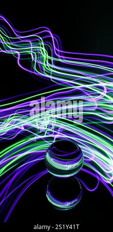 Tourbillons de lumière colorée dans une photographie à longue exposition autour d'une boule de verre sur un miroir. Reflets et tourbillons de fond clair Banque D'Images