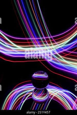 Tourbillons de lumière colorée dans une photographie à longue exposition autour d'une boule de verre sur un miroir. Reflets et tourbillons de fond clair Banque D'Images