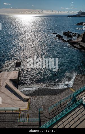 Une scène pittoresque avec un littoral aux eaux bleues limpides, des formations rocheuses et des reflets du soleil. L'ambiance sereine est complétée par con Banque D'Images