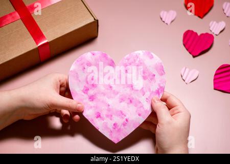 Carte de voeux de Valentines rose dans les mains de la femme. Carte faite à la main pour la Saint-Valentin. Copier l'espace sur fond rose. Concept de la Saint-Valentin Banque D'Images