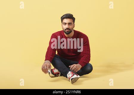 Un modèle masculin asiatique posant en pull rouge sur fond jaune dans le style Banque D'Images