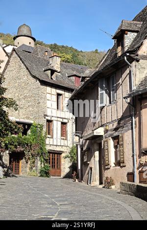 Charmante rue de Conques avec des bâtiments en pierre pittoresques et le soleil illuminant l'architecture historique. Banque D'Images